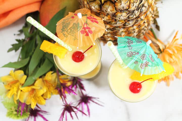 Overhead of cream of coconut cocktails by pineapples and flowers.