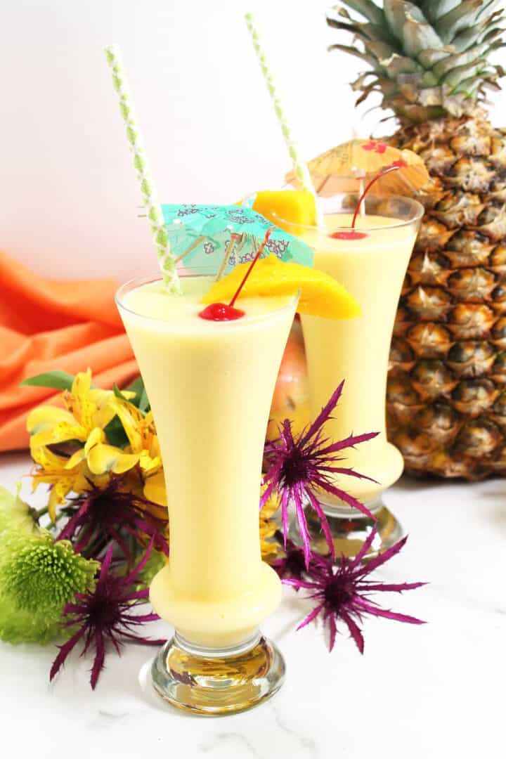 Two mango coladas garnished with cherry among flowers.