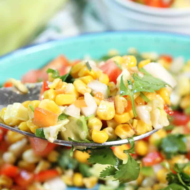 Closeup of spoonful of corn and avocado salad over serving bowl.