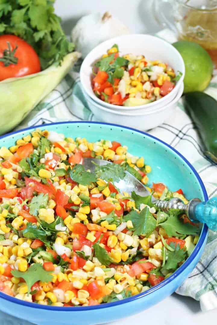 Roasted Corn Salad in bowl with serving spoon and serving bowls in back.
