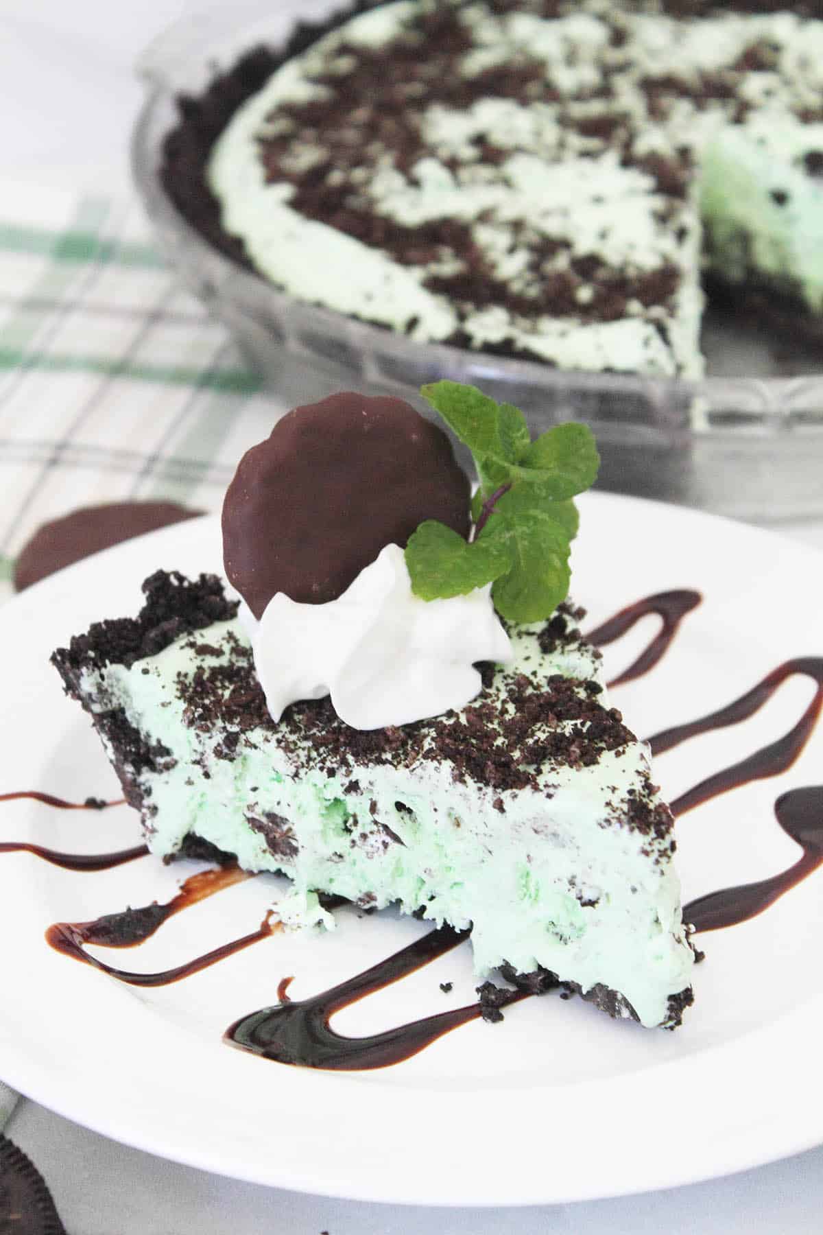 Slice of grasshopper pie on chocolate decorated plate with whole pie in back.
