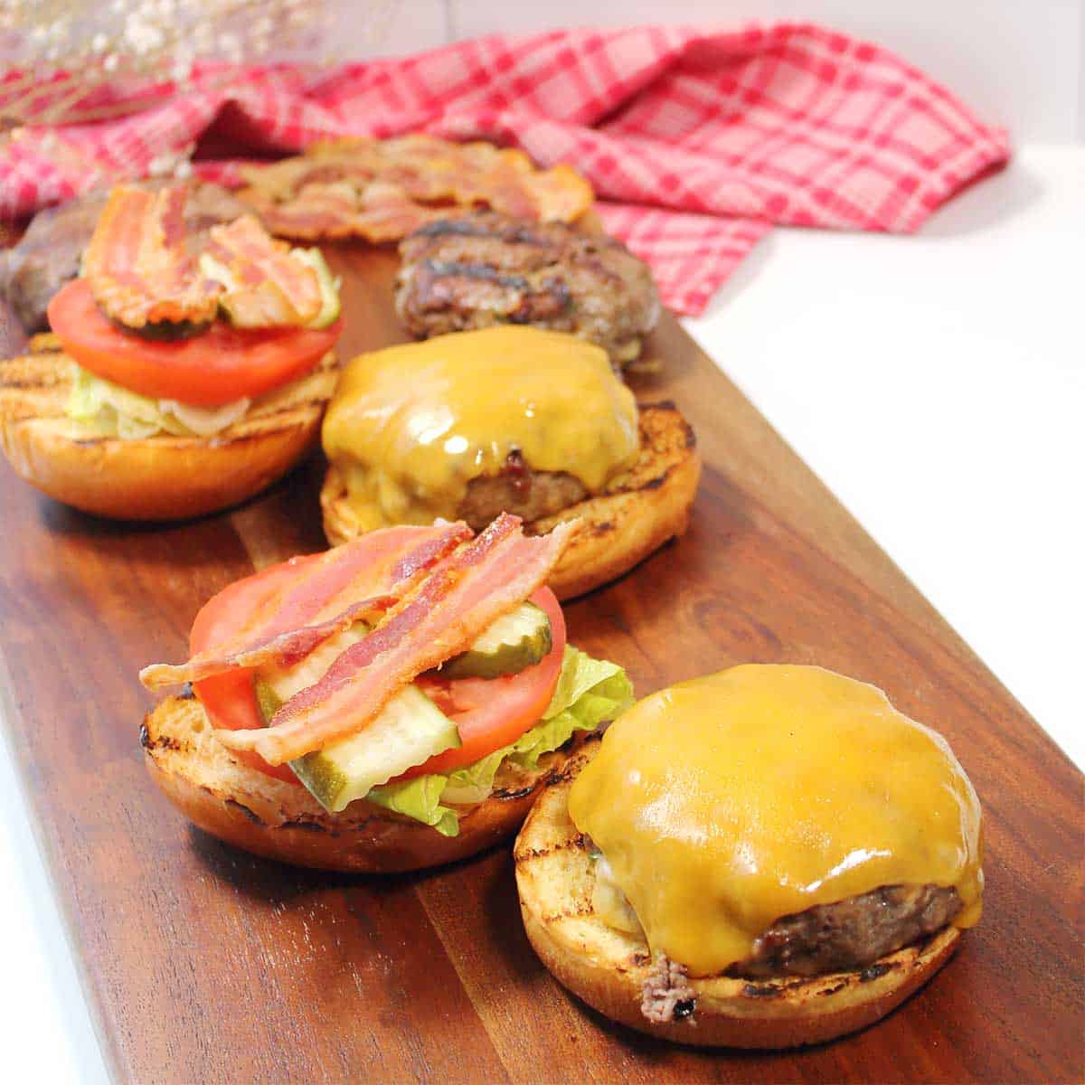Burgers on wooden board with toppings.