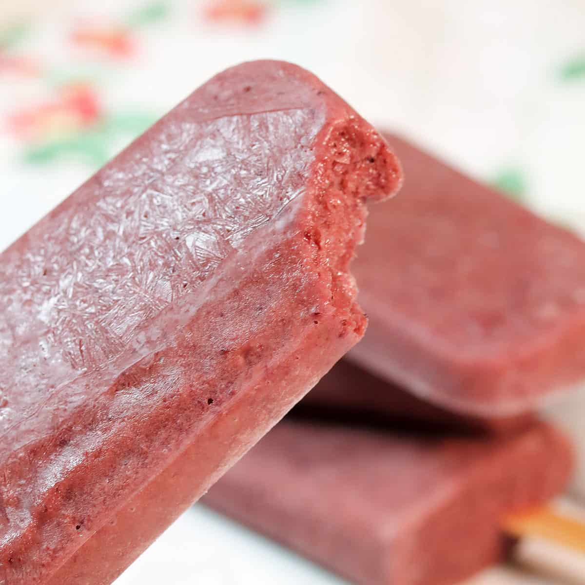 Closeup of cherry popsicle with bite taken out.