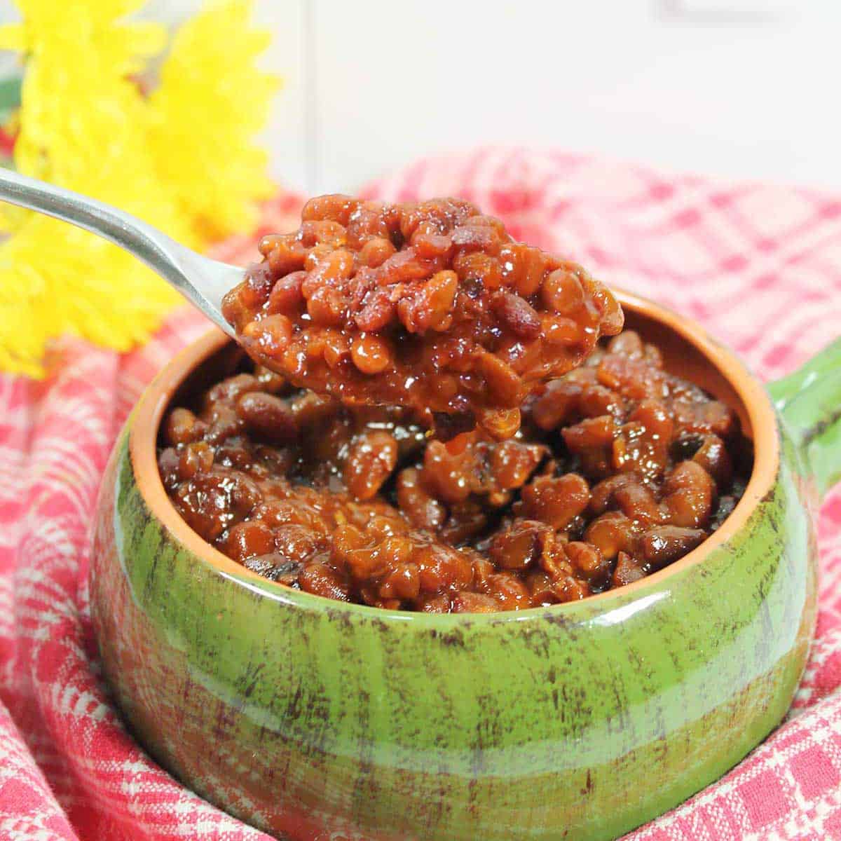 Spoonful of crockpot bourbon baked beans over bowl.