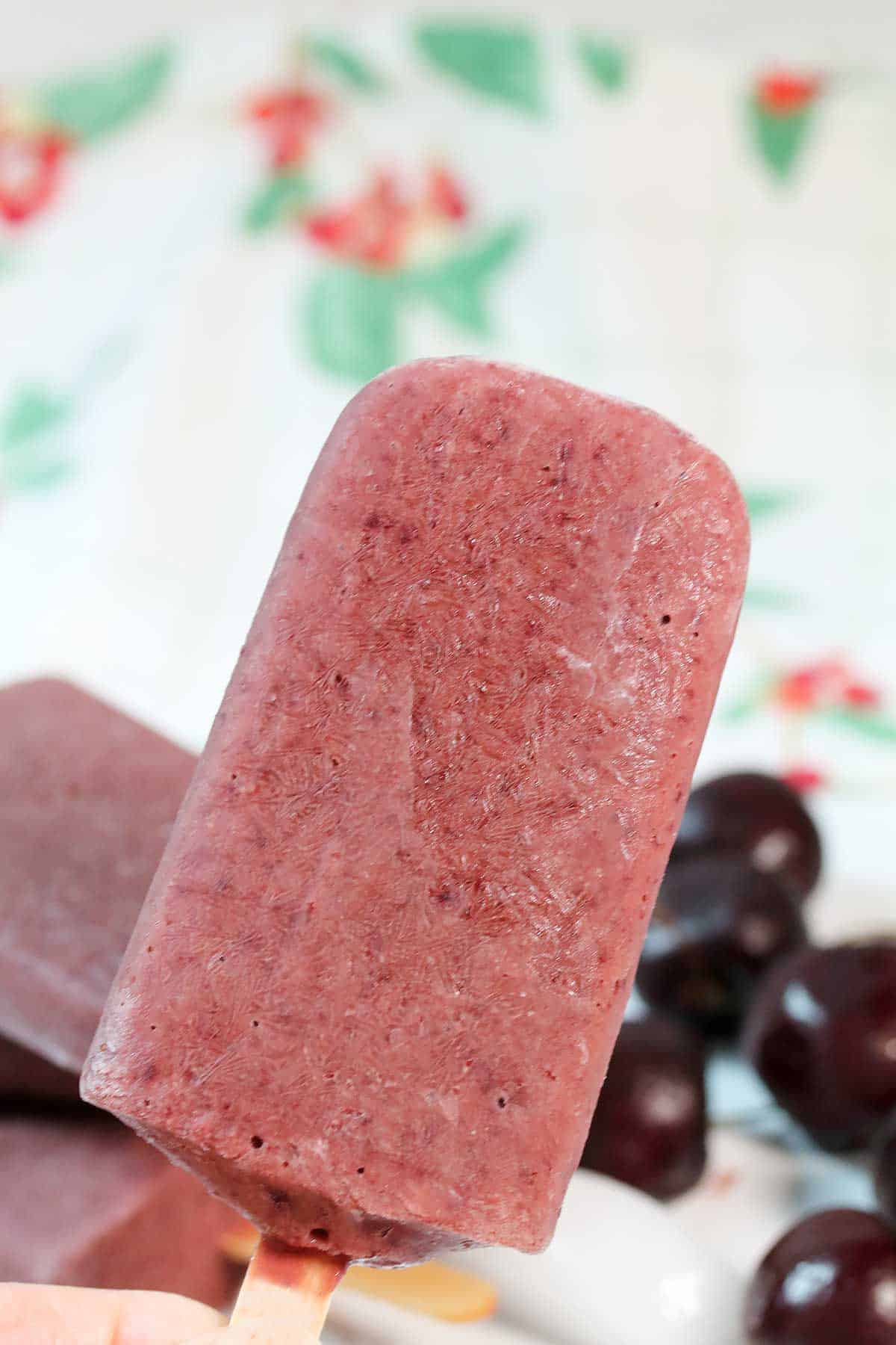 Closeup holding cherry popsicle over cherries.