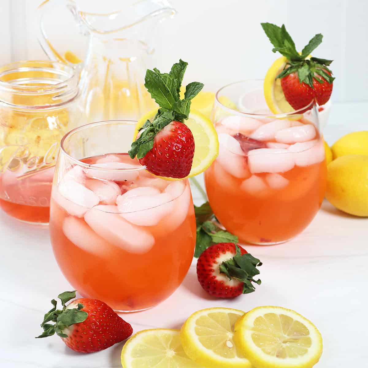 Two Strawberry Lemonade Cocktails with garnishes of strawberry, lemon slice, and mint leaves.