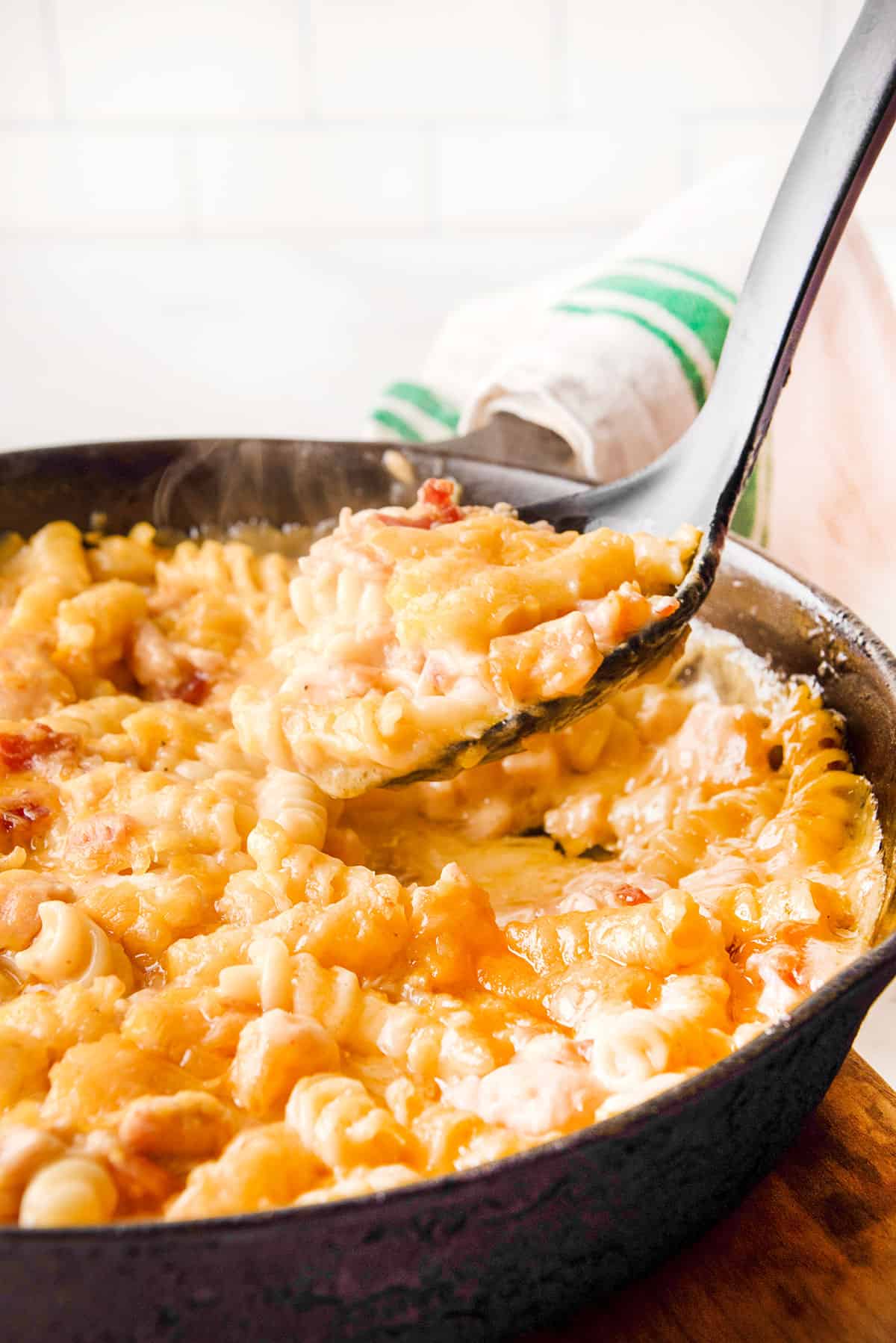 Dishing bacon mac and cheese out of skillet with spoon.