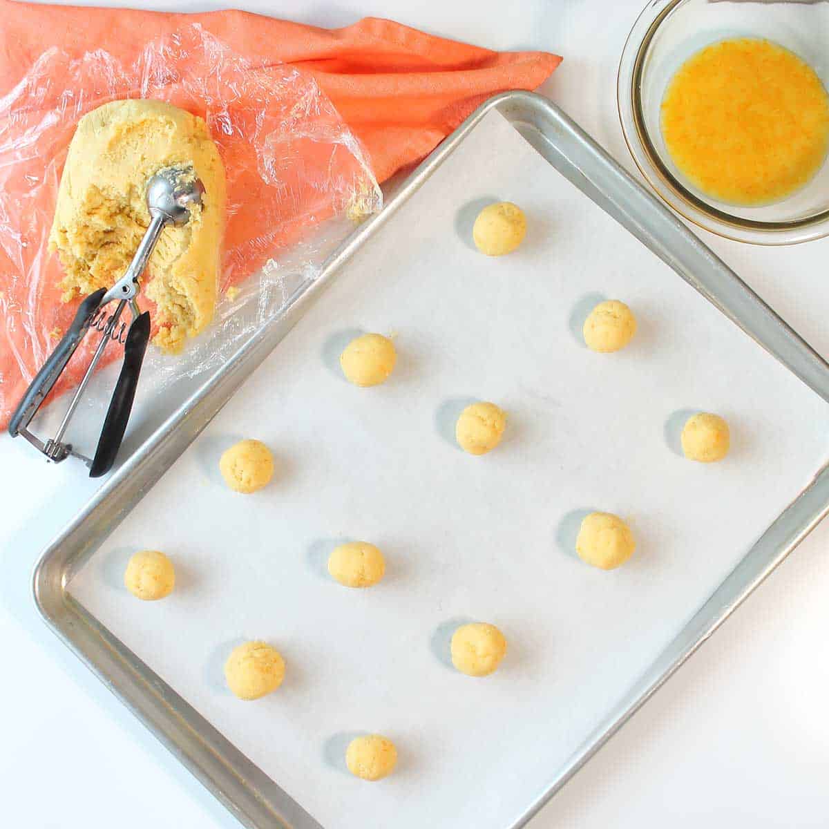 Scooped orange cookie dough on cookie sheet.