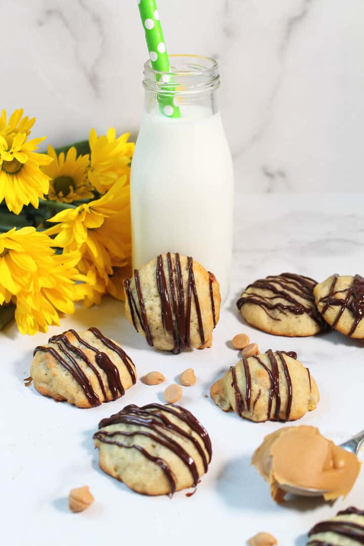 Cookies on white table with one leaning on milk bottle and daisies.