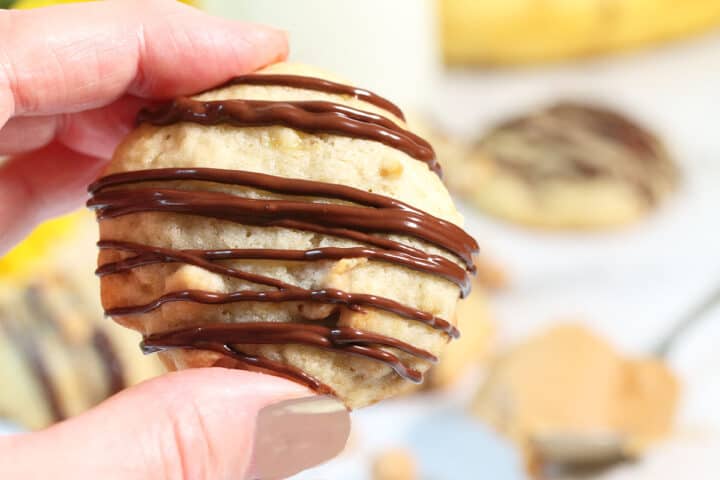 Holding cookie with spoon of peanut butters in background.