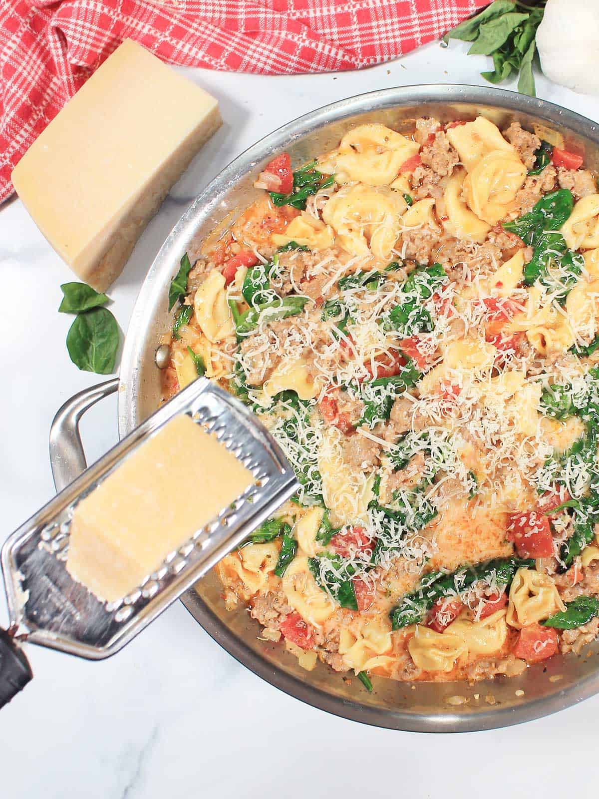 Grating parmesan cheese over tortellini with Italian sausage.