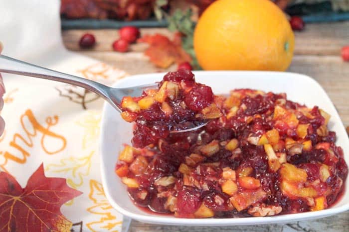 Spoonful of relish over full relish bowl with orange in background.