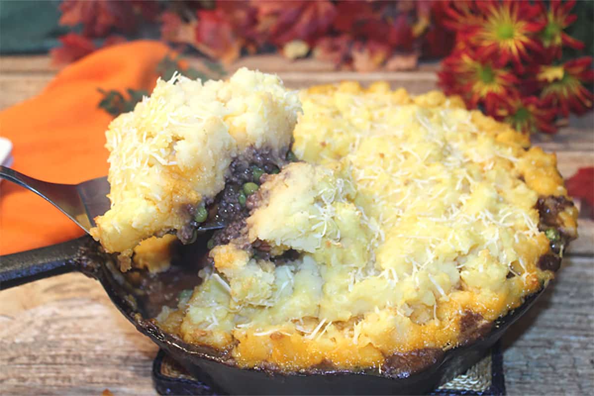 Lifting a serving of pie out of iron skillet showing filling and browned potatoes.