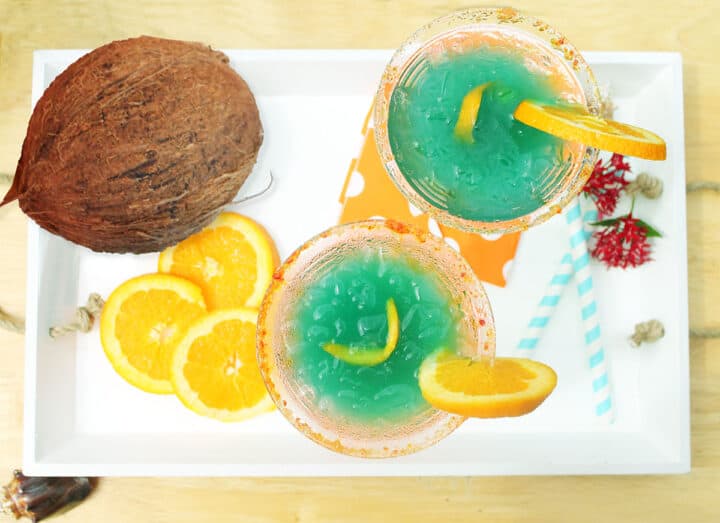 Overhead of two tropical cocktails with coconut on white tray.