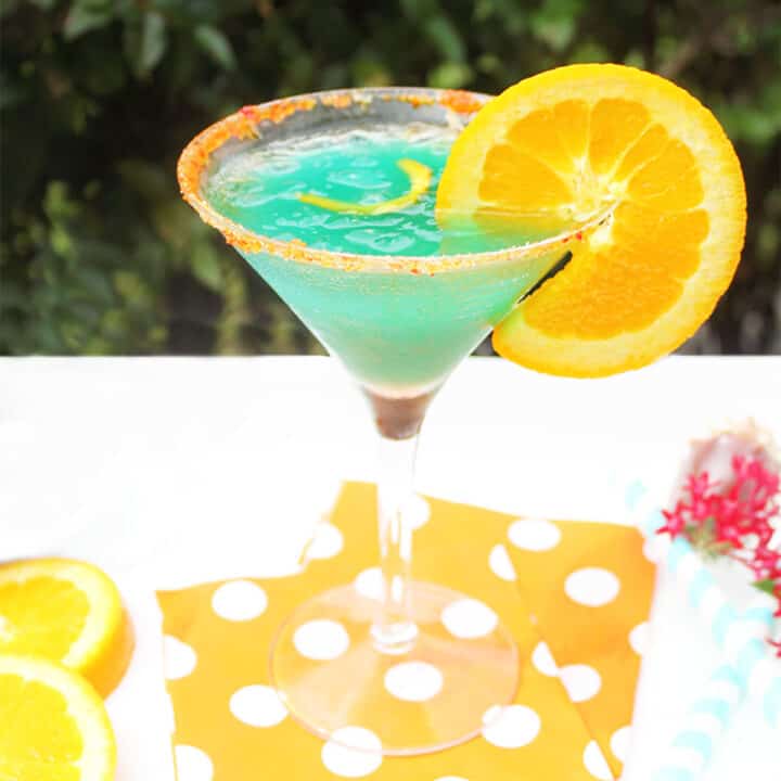 Single curacao cocktail on orange polka dotted napkins.