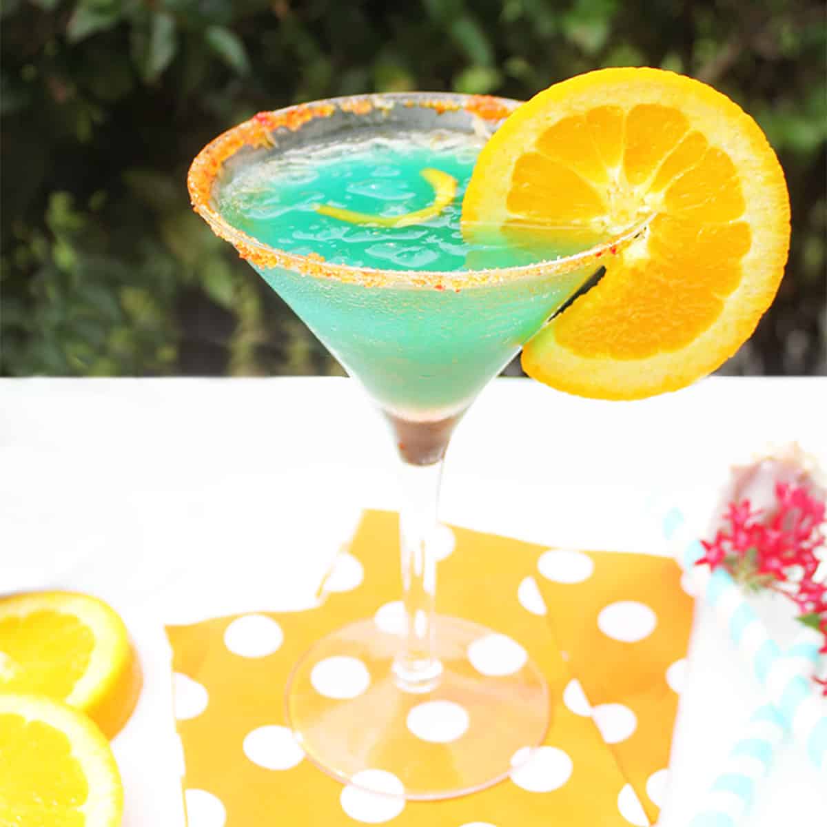 Single curacao cocktail on orange polka dotted napkins.