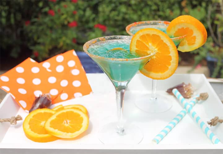 Two blue cocktails on wooden tray with striped straws.