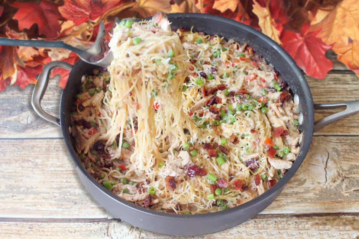 Lifting pasta out of skillet with fall leaves in back.