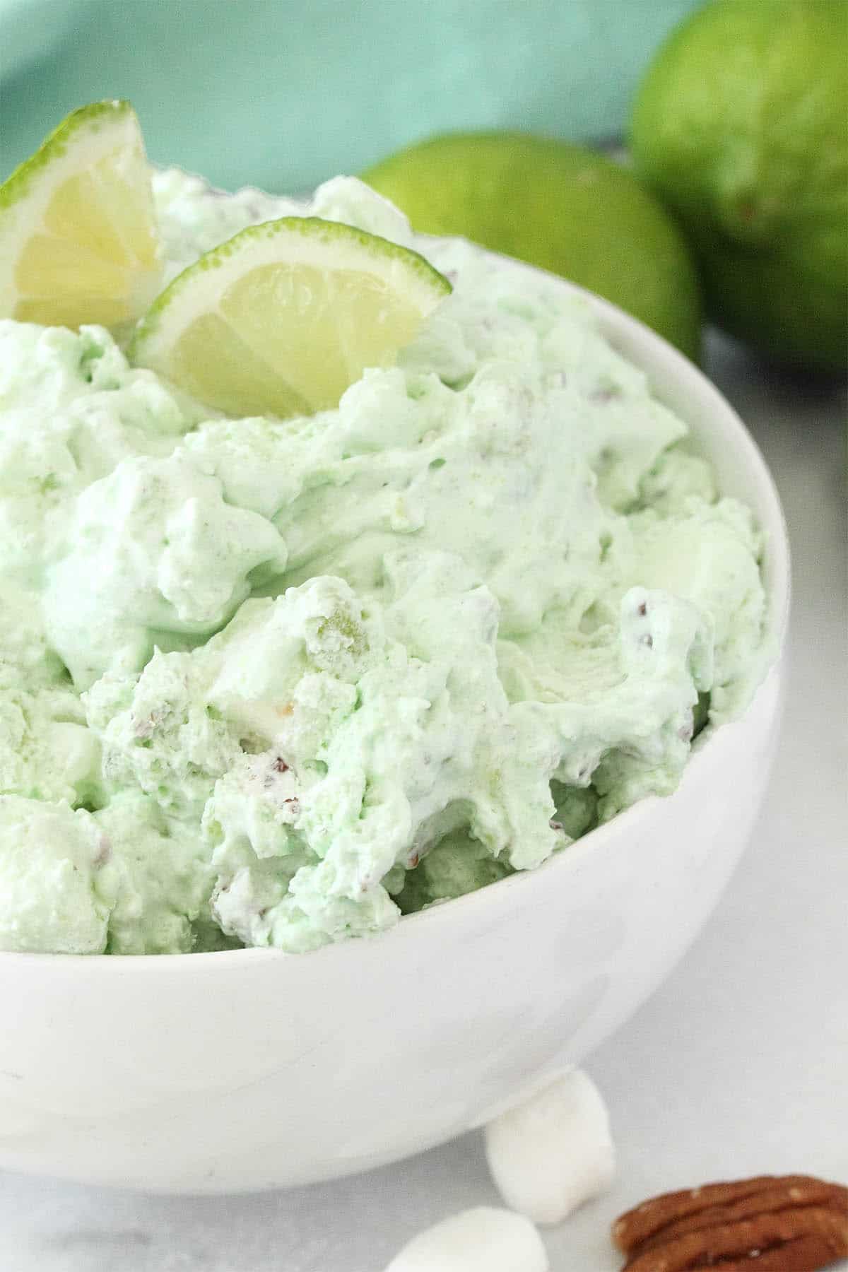 Partial view of bowl of green fluff with two limes on top.