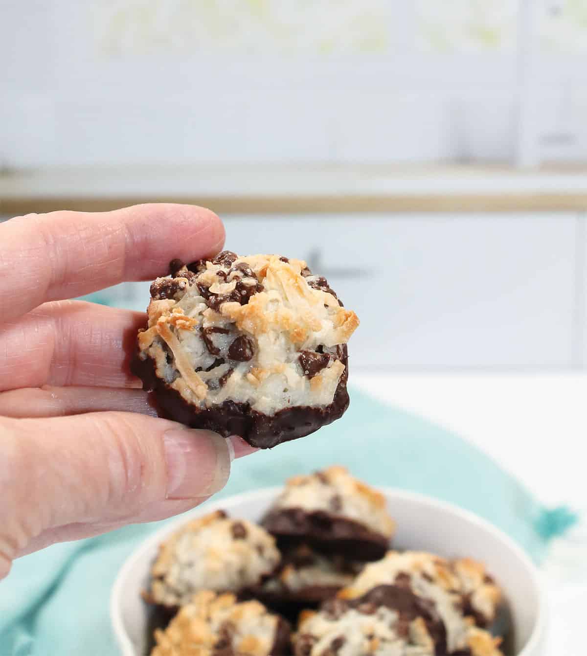 Holding chocolate cipped coconut macaroon over bowl.