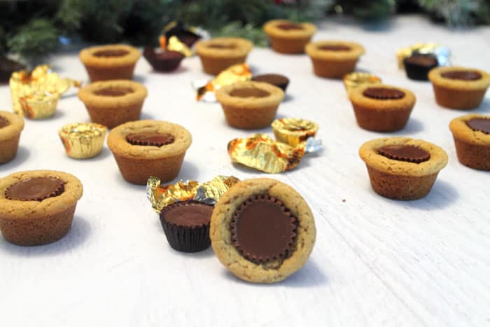 Scattered Peanut Butter Cup Cookies on white table with candy around them.