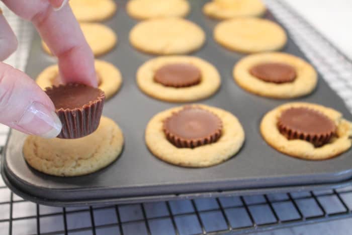 Pressing peanut butter cup into center of warm cookies.