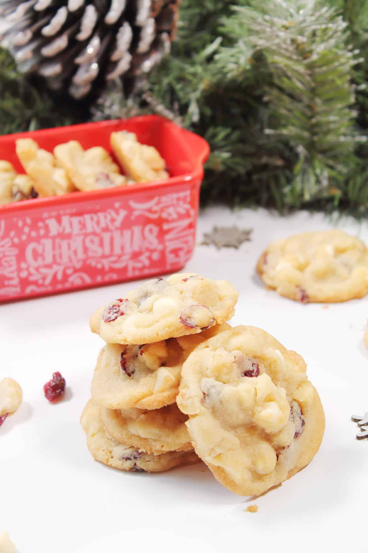 Stack of white chocolate cranberry nut cookies in front of Christmas dish.