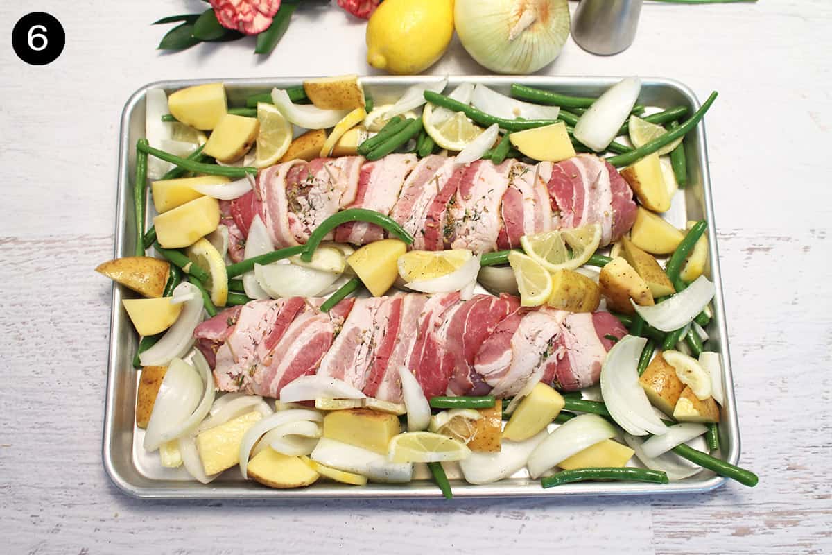 bacon wrapped tenderloin on sheet pan surrounded by potatoes and vegetables.