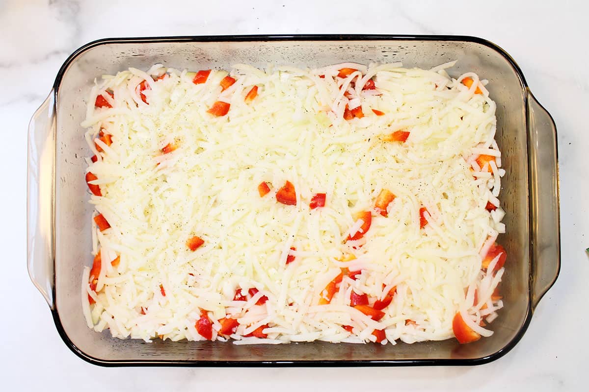 Potatoes onions and peppers pressed into casserole dish.