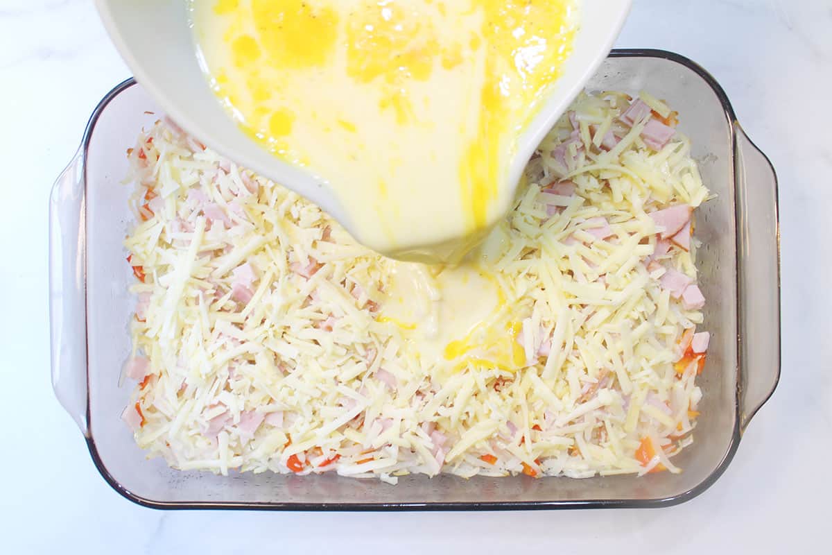 Pouring egg mixture over layered casserole.