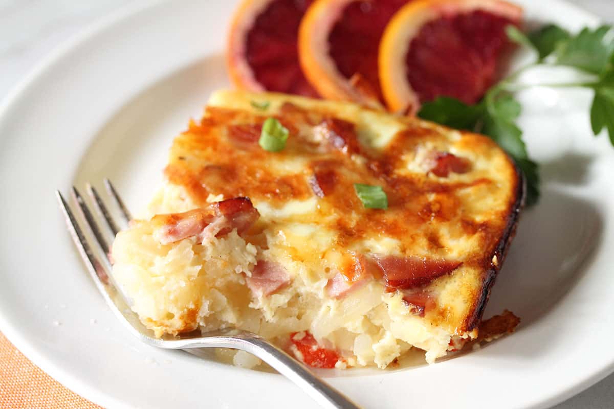 Slice of casserole on white plate with bite on fork.