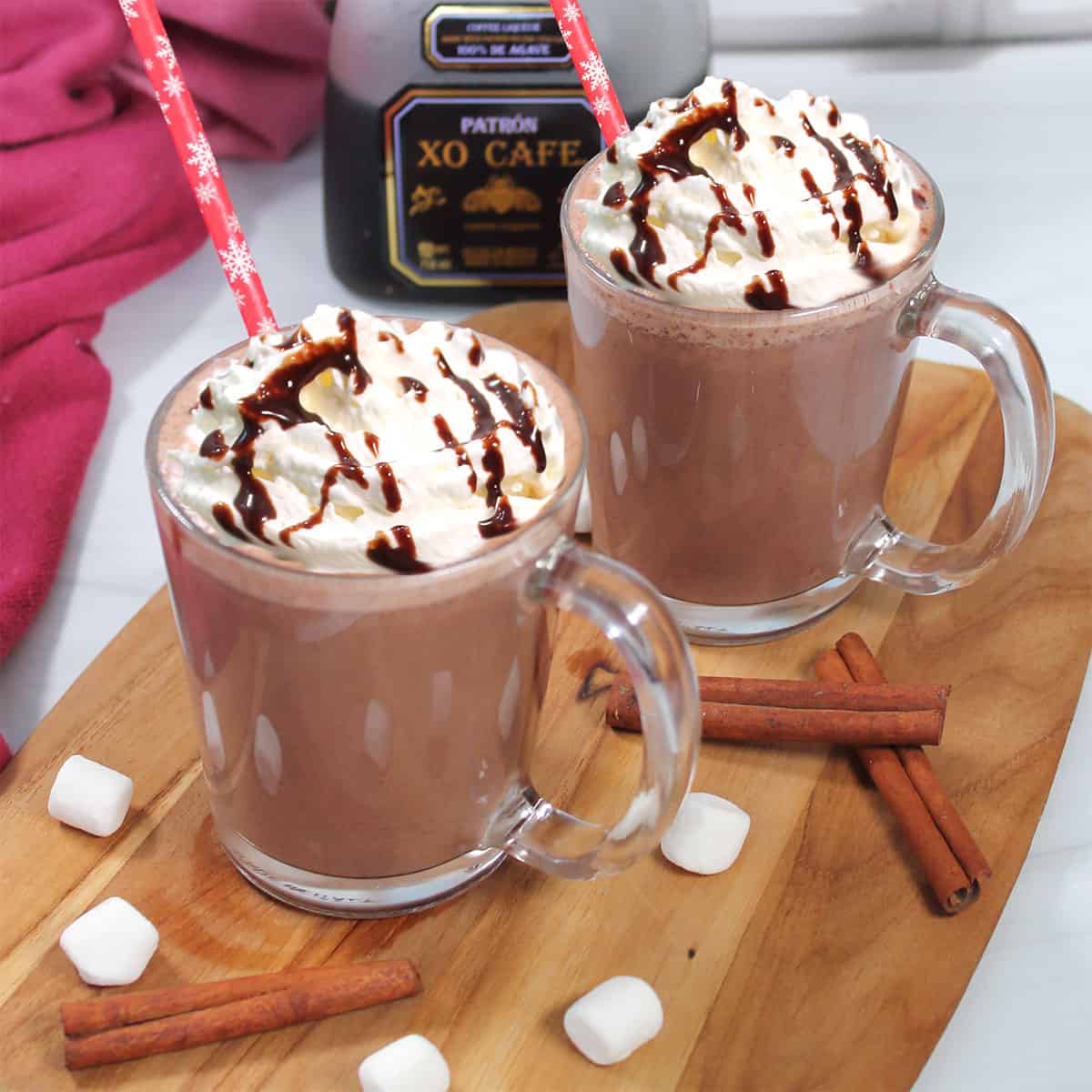 Two mugs of Spiked Mexican Hot Chocolate with tequila bottle in back.
