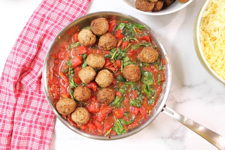 Adding meatballs to tomato sauce in skillet.