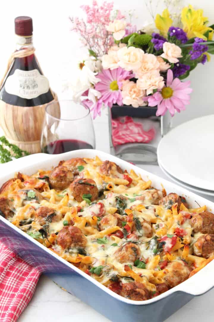 Baked meatball casserole with wine and flowers behind it.