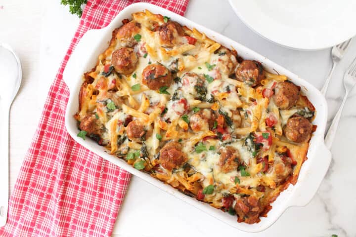 Baked pasta with meatballs casserole on white table with red checkered towel.