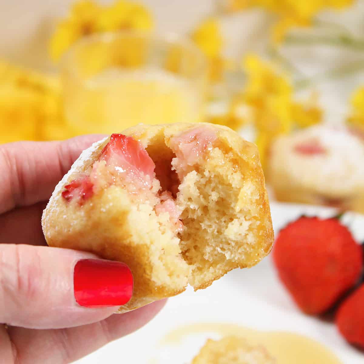 Holding muffin with strawberries with bite out of it.