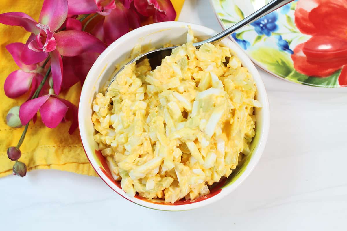 Overhead of bowl of homemade egg salad next to pink flowers.
