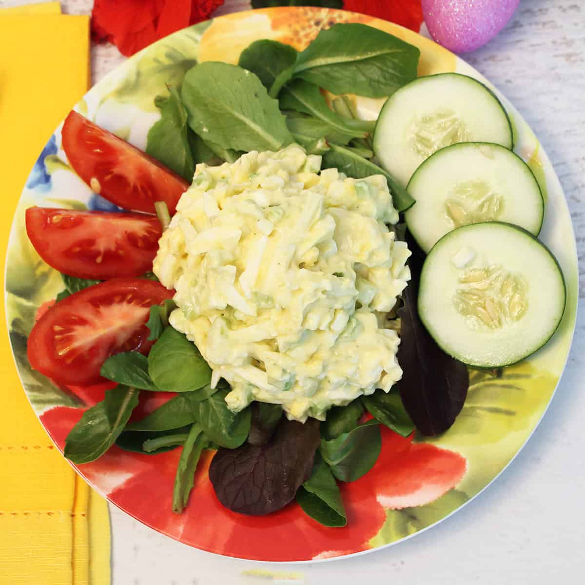 Overhead of salad on floral plate with tomatoes and cucumbers.