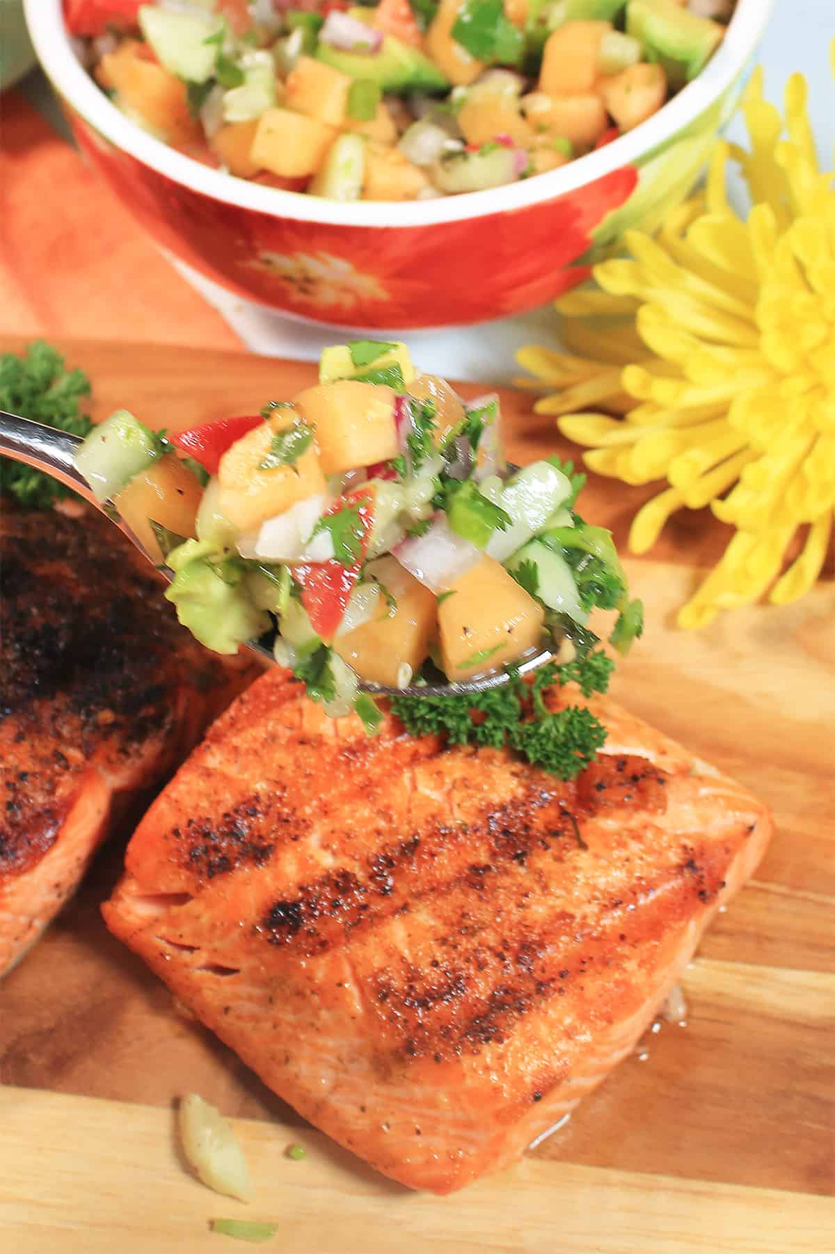 Spoonful of salsa with cucumber over grilled salmon.