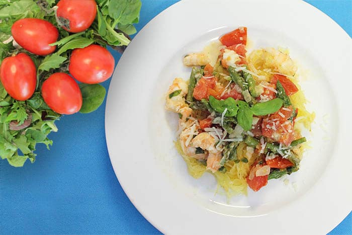 Shrimp Primavera on a white plate with blue placemat and tomatoes on the side
