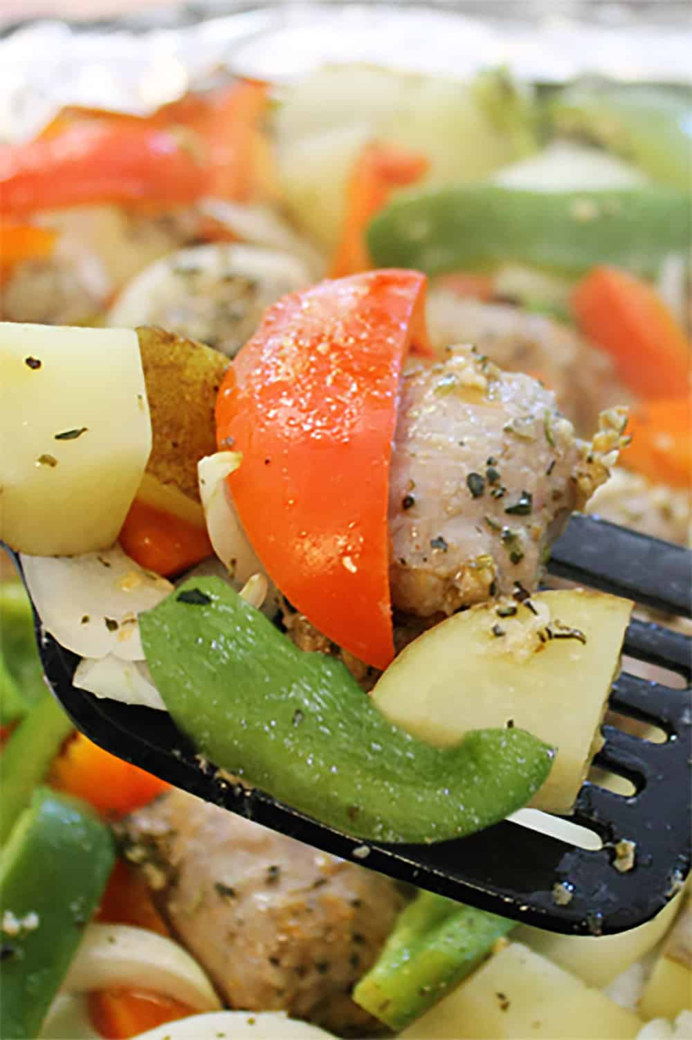 Closeup of baked sausage and peppers and potatoes on spatula.