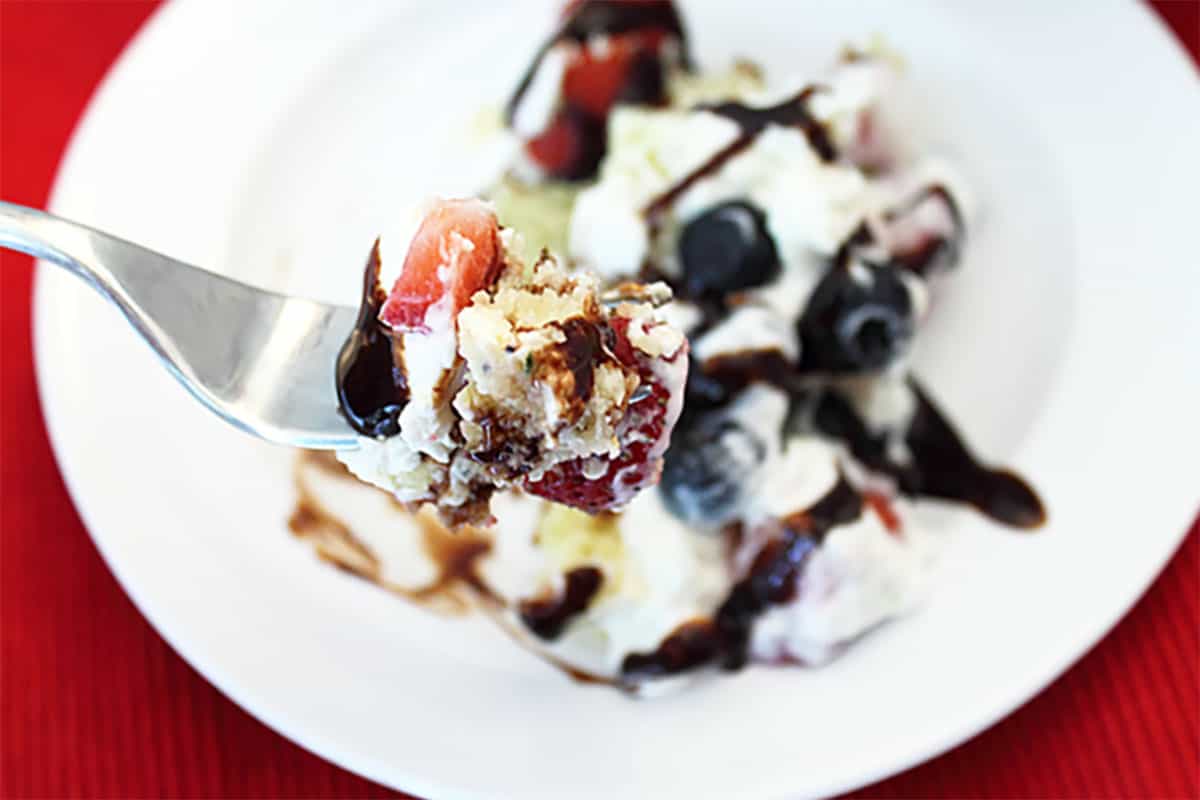 Bite on fork above serving of trifle drizzled with chocolate syrup.