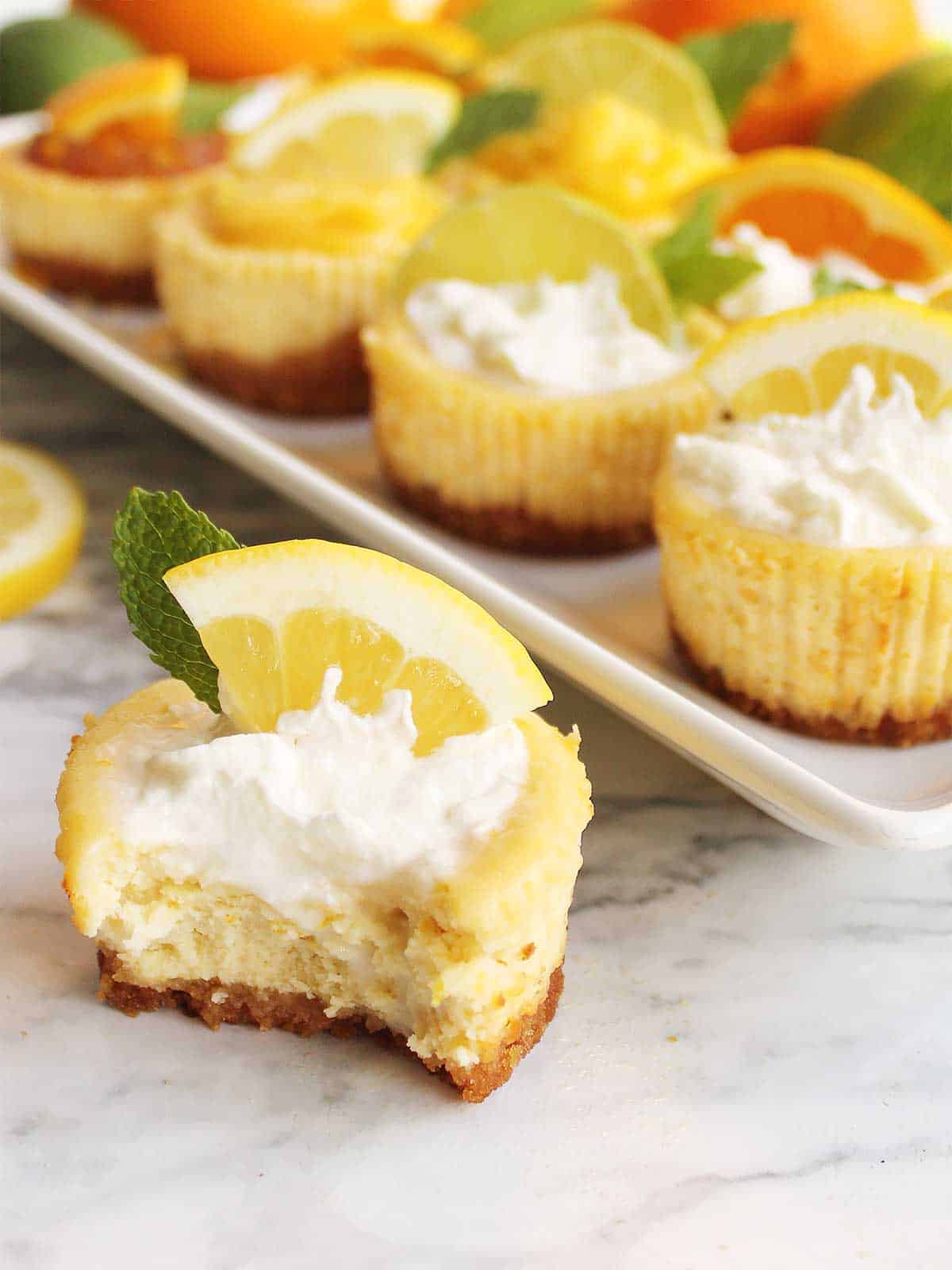 Mini cheesecakes with bite out of one in front of platter.