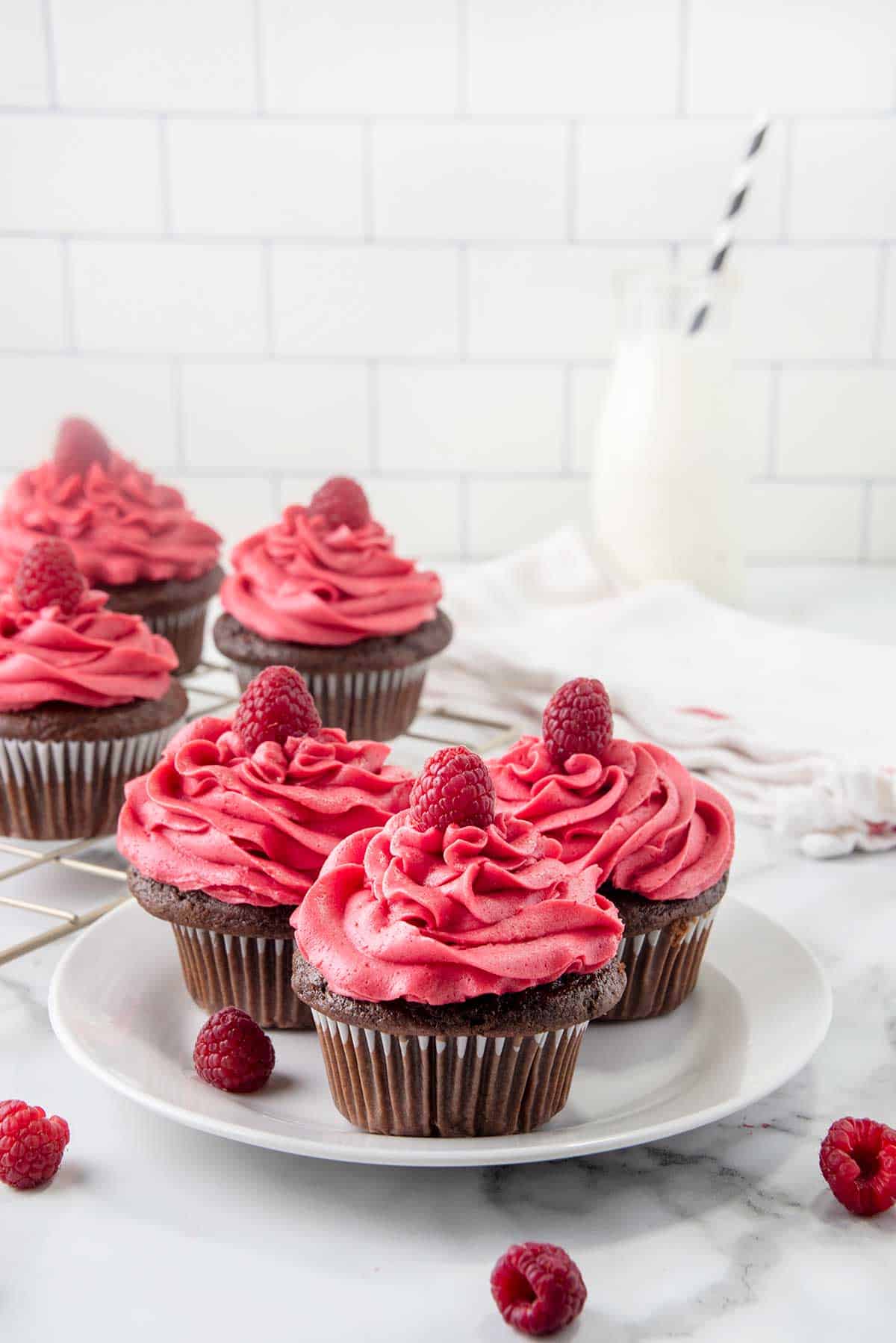 Three frosted cupcakes on plate with milk bottle in back.