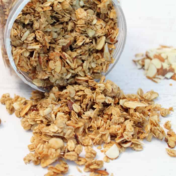 Granola spilling out of container showing crunchy oats, nuts and coconut.