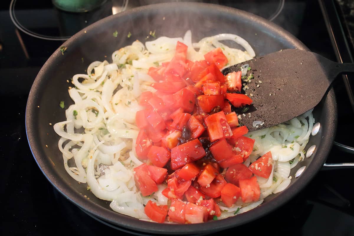 Adding tomatoes to skillet with onions.