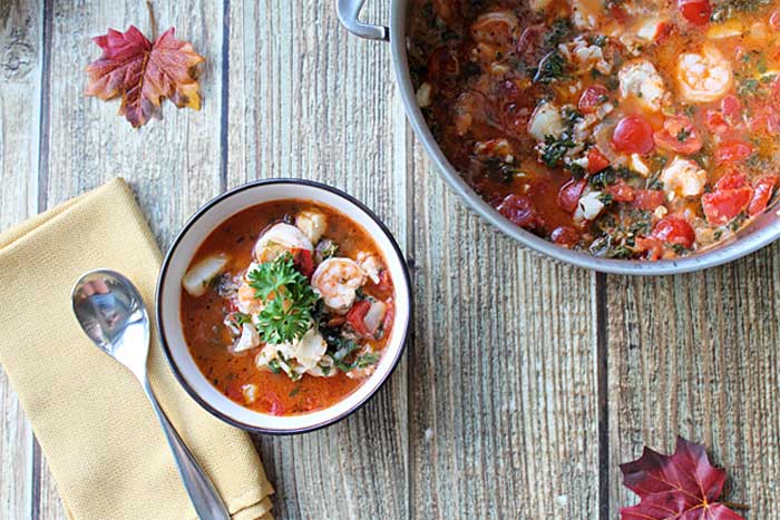 overhead of bowl and pot of stew on wooden table with gold napkin and fall leaves.