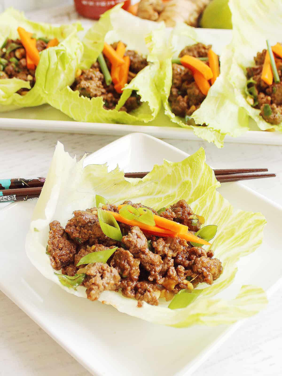 Plated Asian lettuce wraps with ground beef in front of platter.
