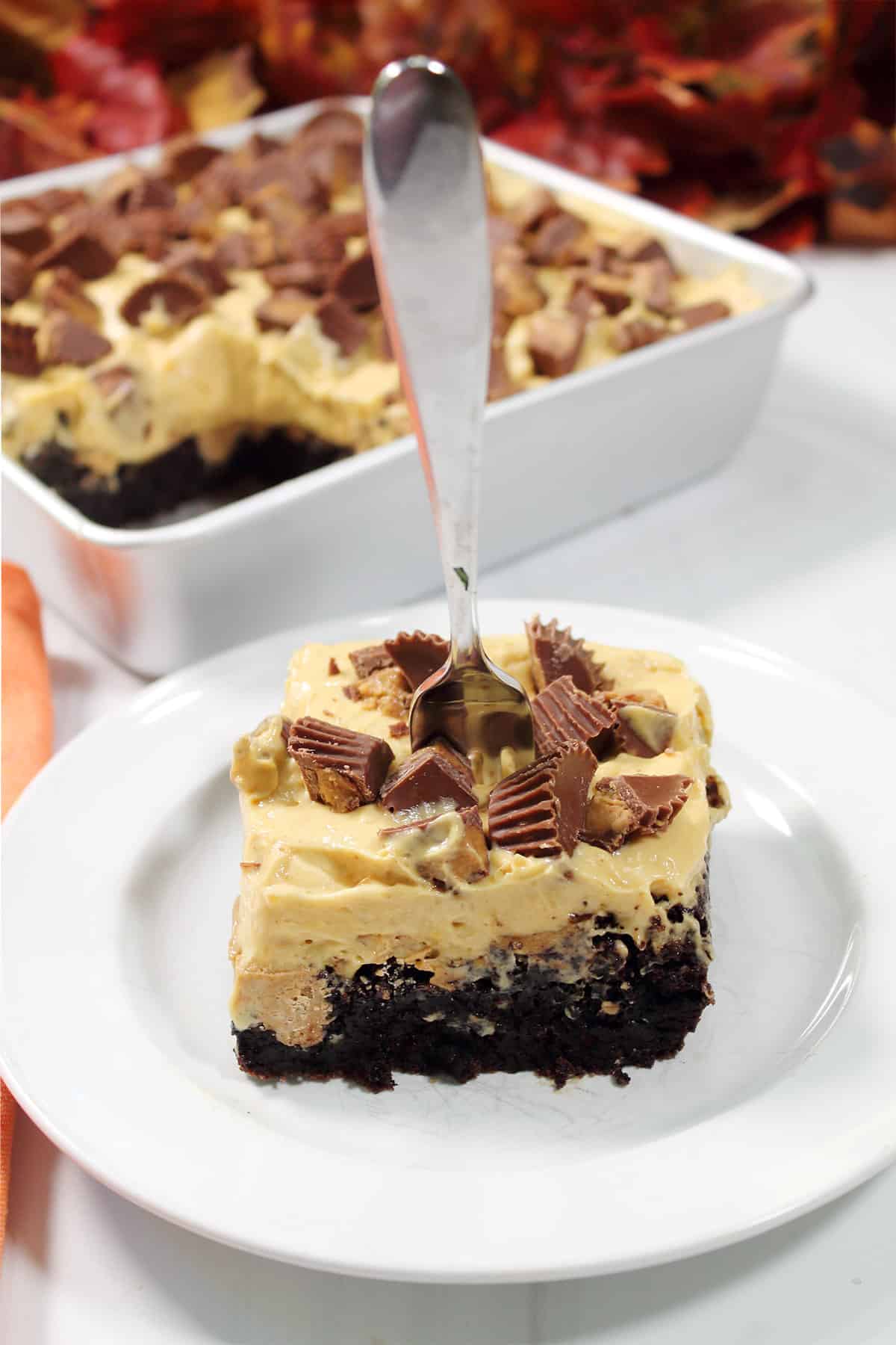 Chocolate Peanut Butter Poke Cake on plate with baking dish in back.