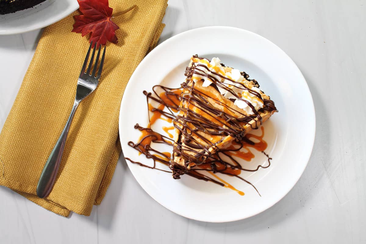 Slice of cheesecake with caramel and chocolate drizzle.